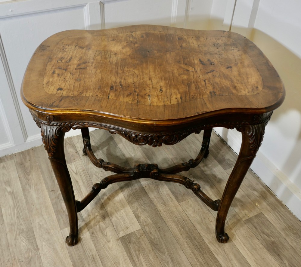 An antique carved walnut occasional table featuring a shaped serpentine top, cabriole legs, and an ornamental carved X-frame stretcher. View II