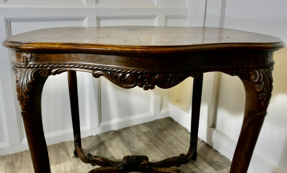 An antique carved walnut occasional table featuring a shaped serpentine top, cabriole legs, and an ornamental carved X-frame stretcher. View III