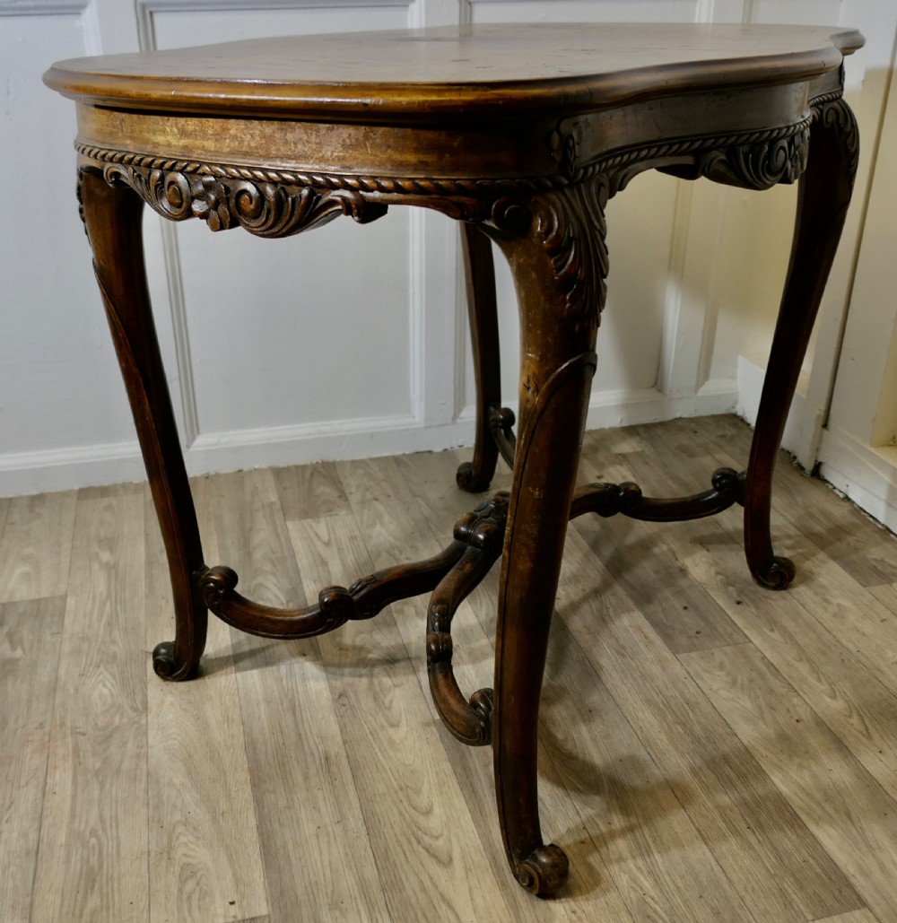 An antique carved walnut occasional table featuring a shaped serpentine top, cabriole legs, and an ornamental carved X-frame stretcher. View V