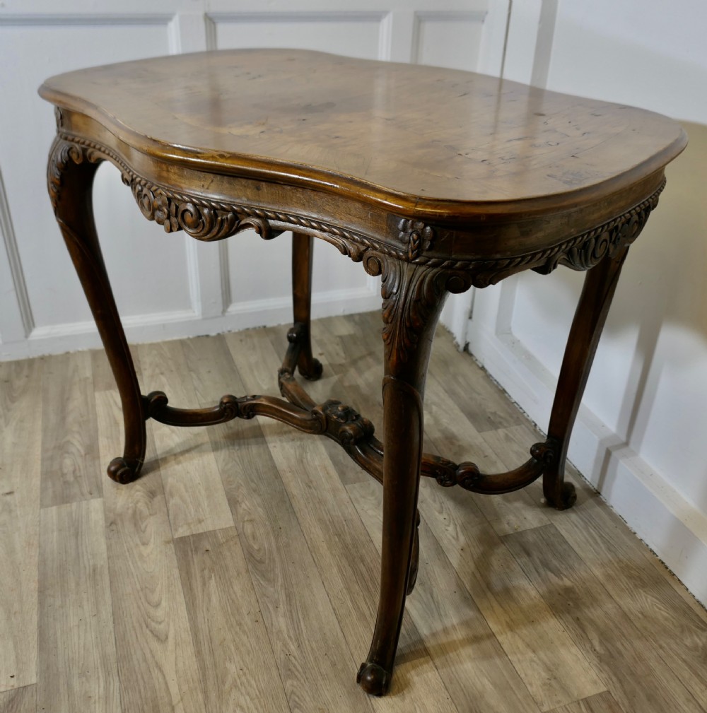 An antique carved walnut occasional table featuring a shaped serpentine top, cabriole legs, and an ornamental carved X-frame stretcher. View VII