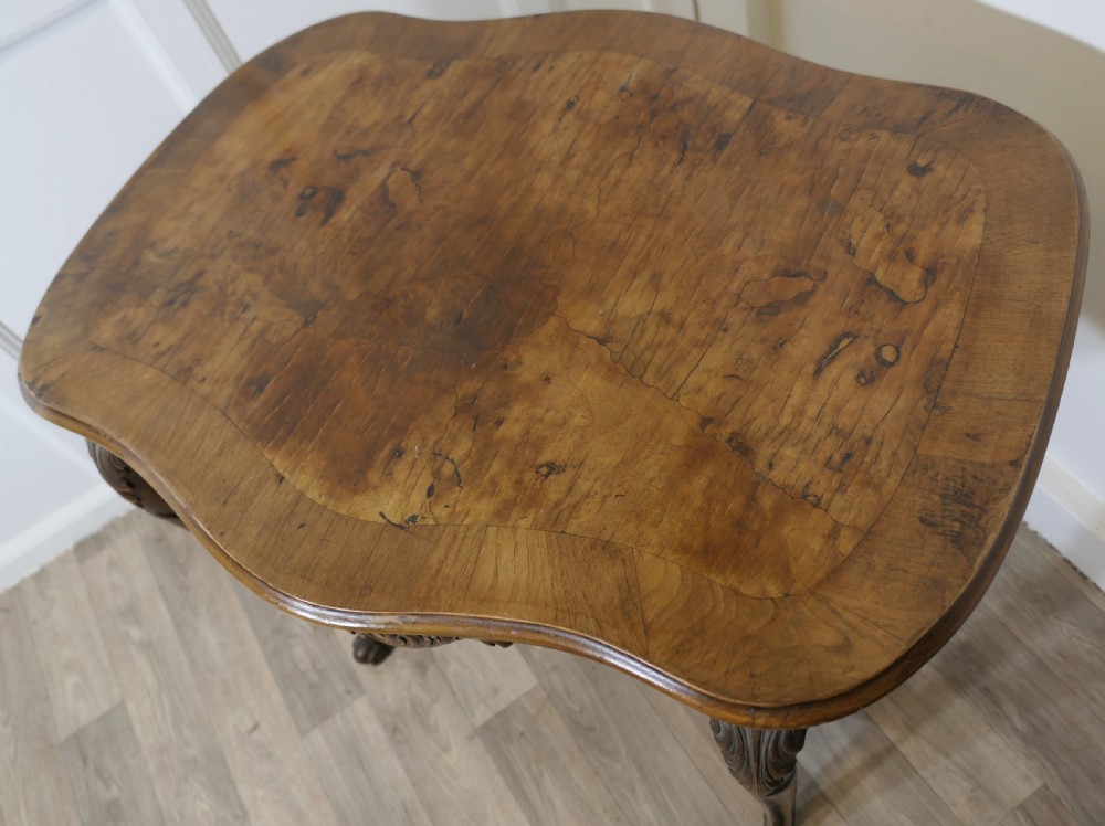 An antique carved walnut occasional table featuring a shaped serpentine top, cabriole legs, and an ornamental carved X-frame stretcher. View VIII