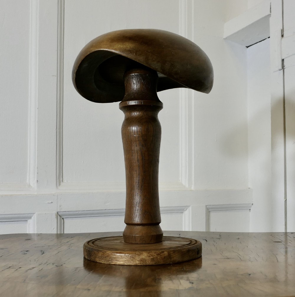 A turned wooden millinery block for a flat cap or beret, featuring a rounded top, a central stem, and a circular base. View III