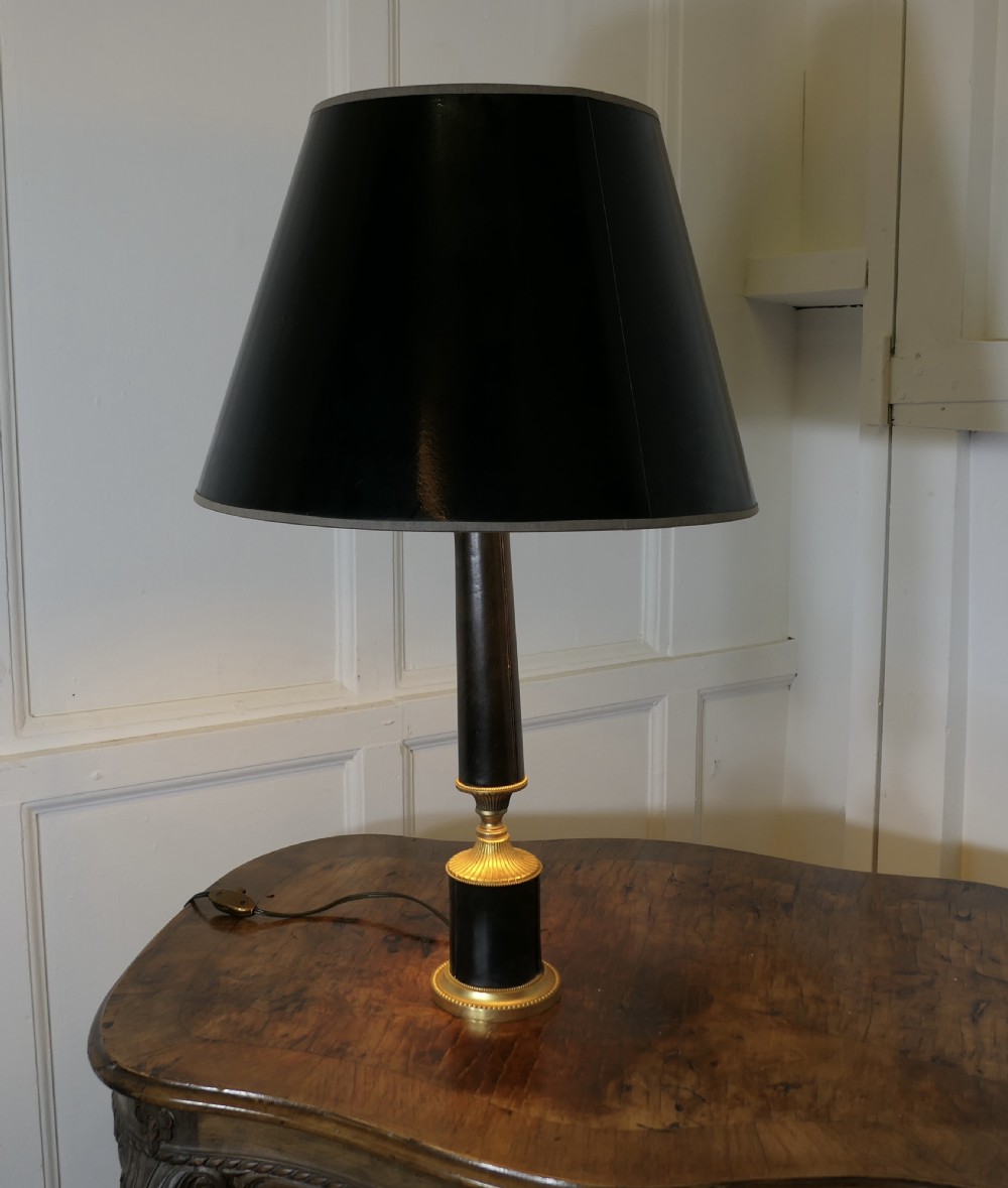 An Art Deco table lamp featuring a tapered black leather stem, a black conical shade, and turned brass fittings.