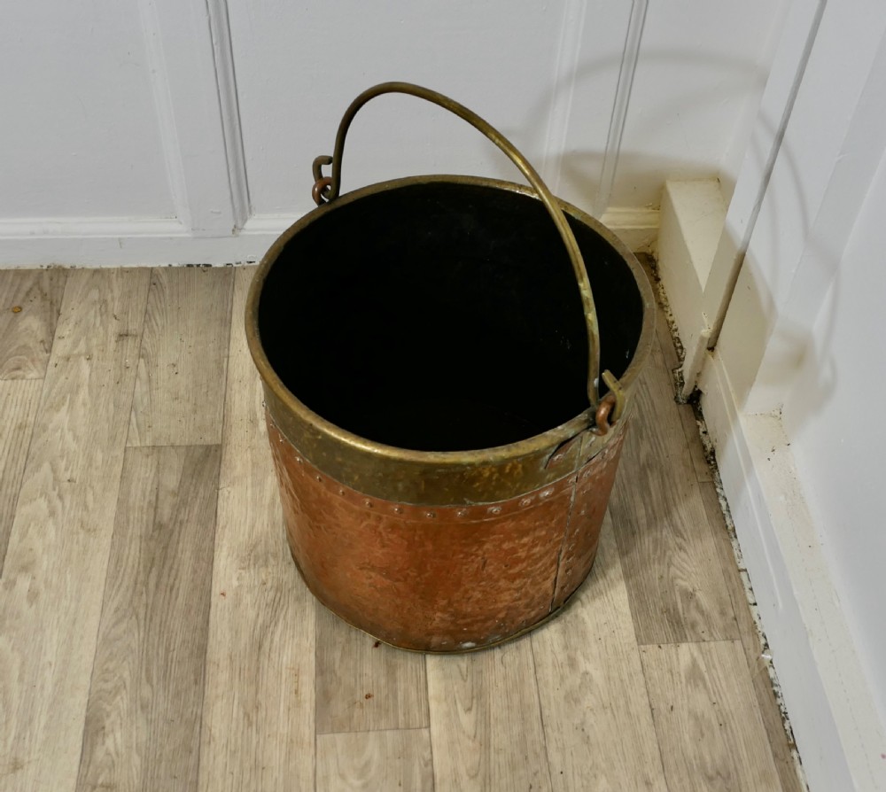 A cylindrical hand-hammered copper bucket featuring a wide brass top collar, riveted seam, and a curved brass swing handle. View VIII