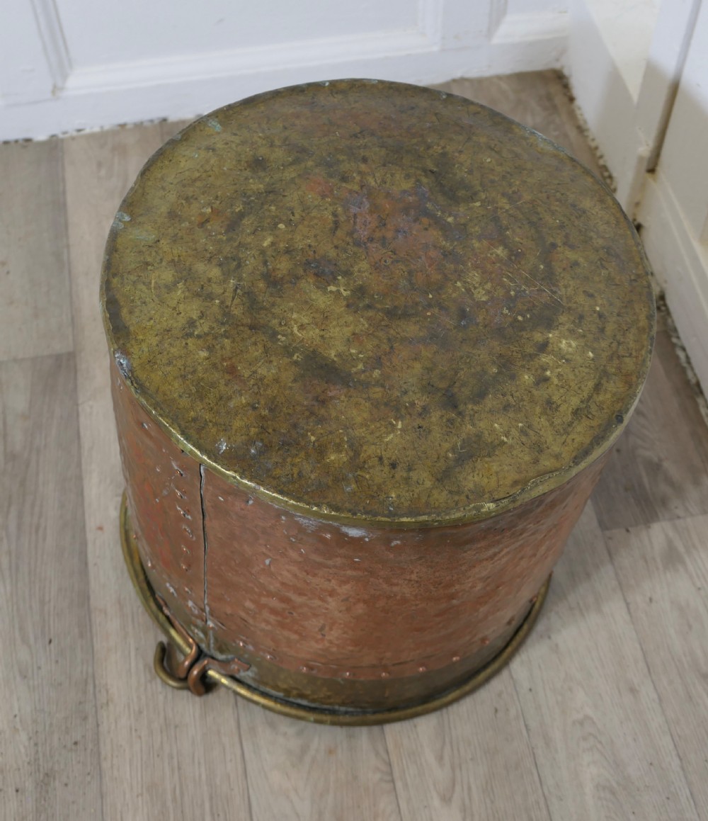 A cylindrical hand-hammered copper bucket featuring a wide brass top collar, riveted seam, and a curved brass swing handle. View XI