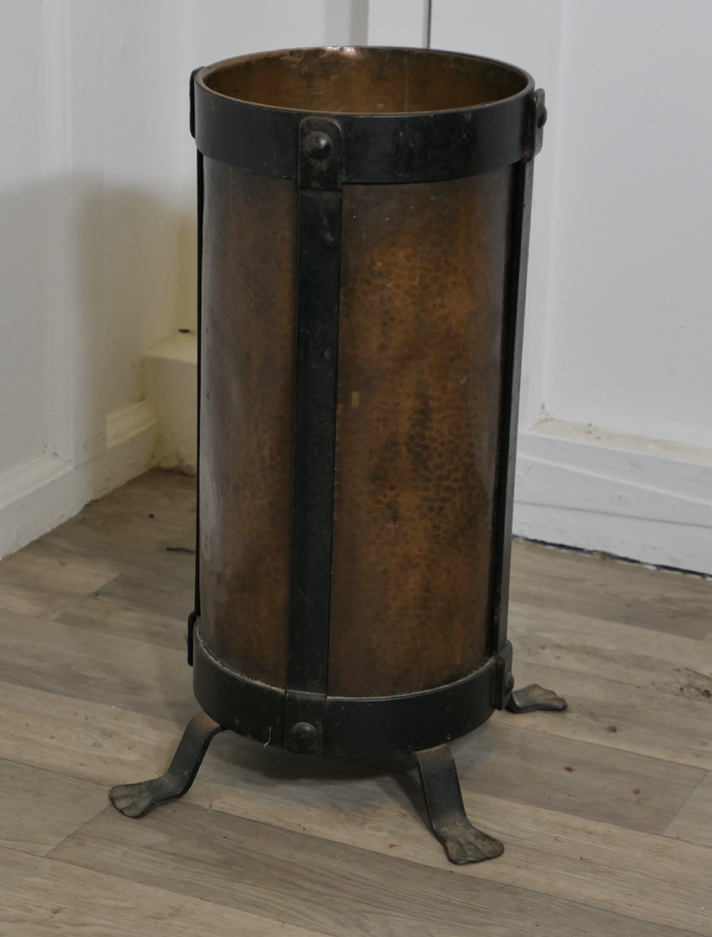 A cylindrical hammered copper stick stand bound with riveted iron straps and resting on iron feet.