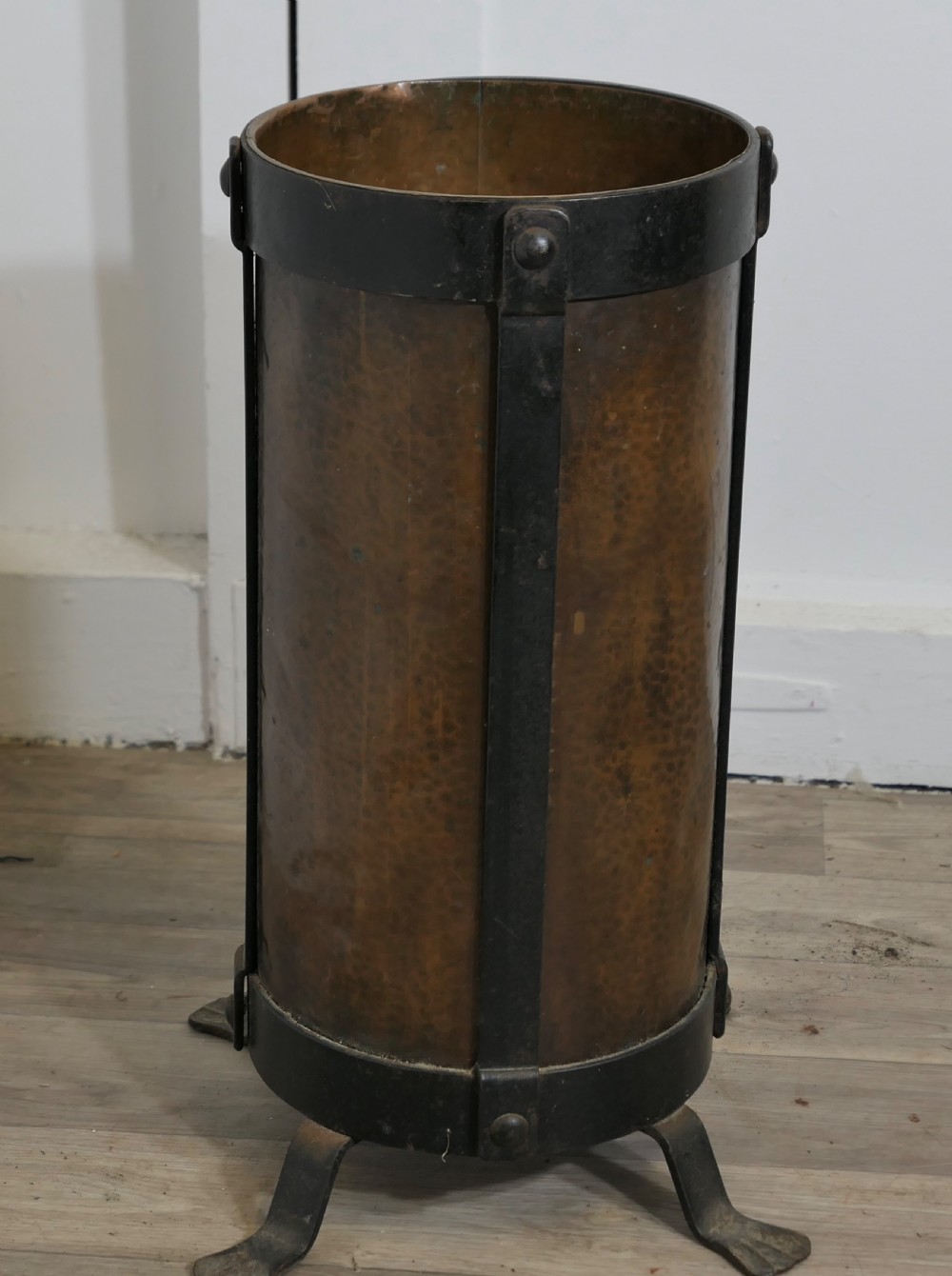 A cylindrical hammered copper stick stand bound with riveted iron straps and resting on iron feet. View II
