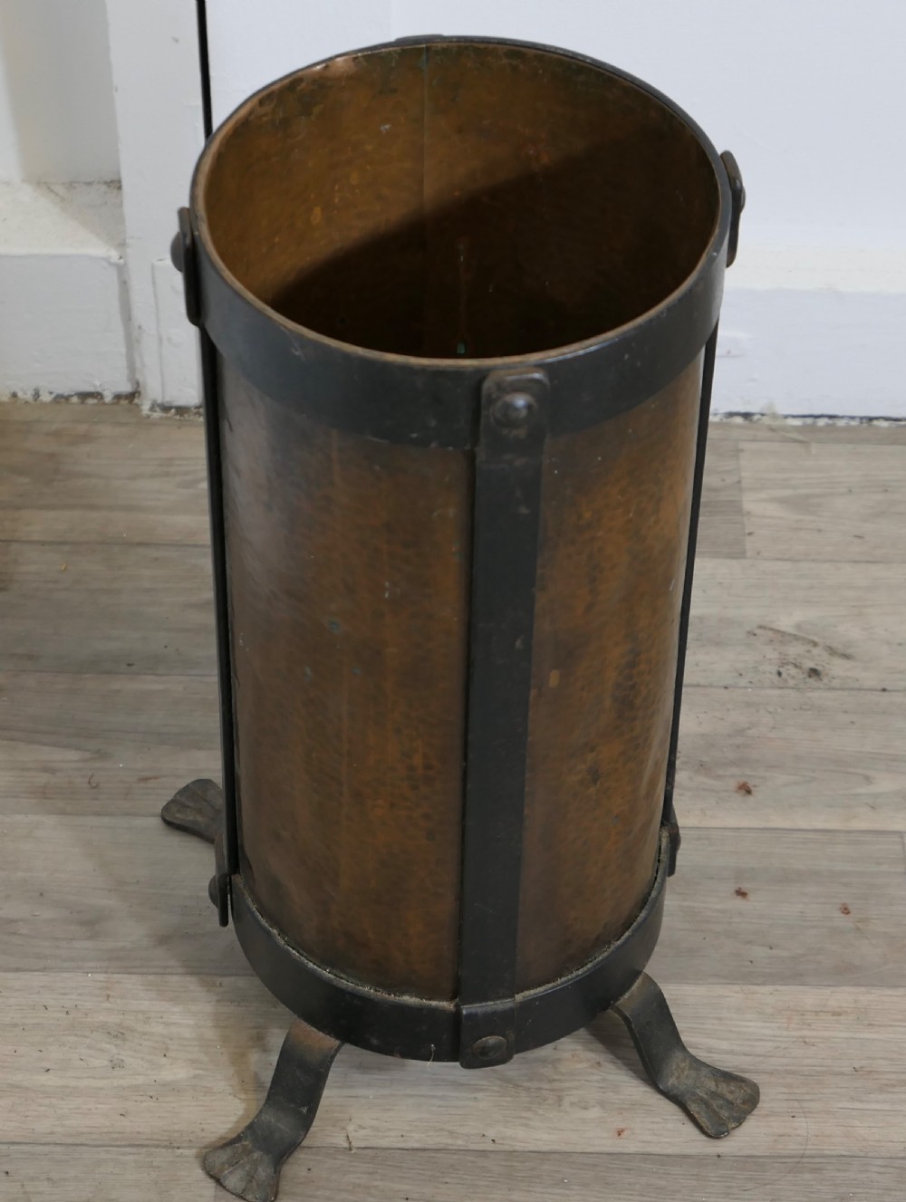 A cylindrical hammered copper stick stand bound with riveted iron straps and resting on iron feet. View III
