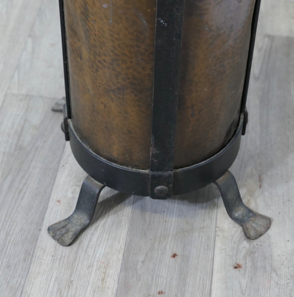 A cylindrical hammered copper stick stand bound with riveted iron straps and resting on iron feet. View IV