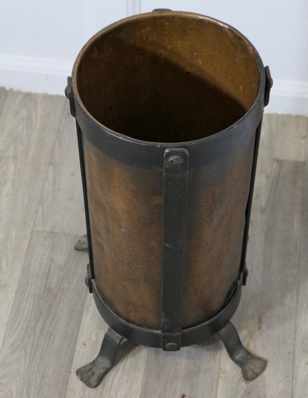 A cylindrical hammered copper stick stand bound with riveted iron straps and resting on iron feet. View V