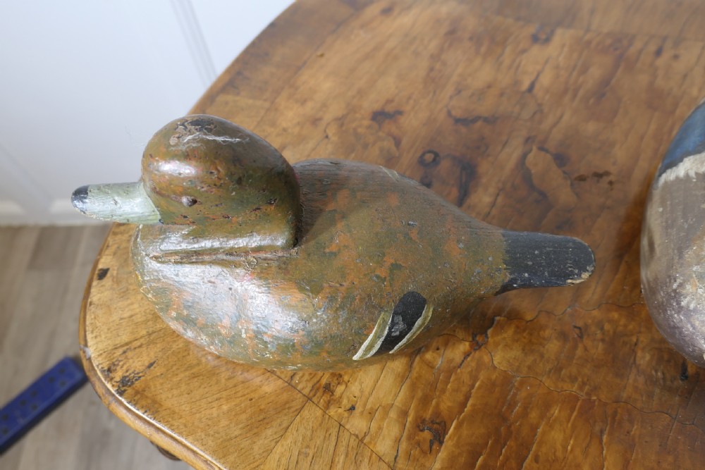Three hand-carved and painted wooden decoy ducks with weathered finishes rest on a polished timber surface. View VI