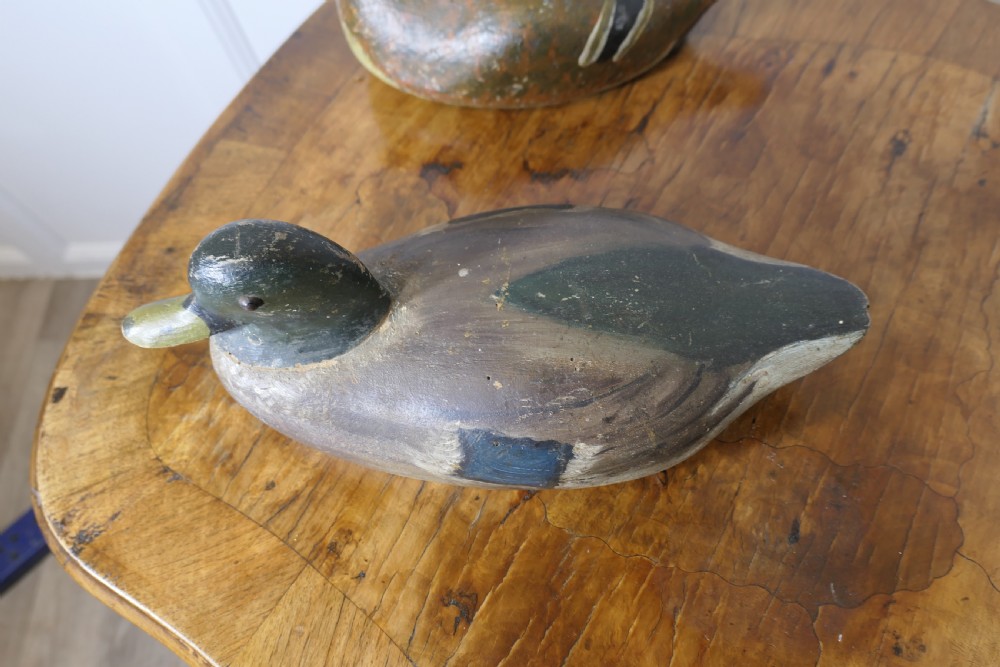 Three hand-carved and painted wooden decoy ducks with weathered finishes rest on a polished timber surface. View VII