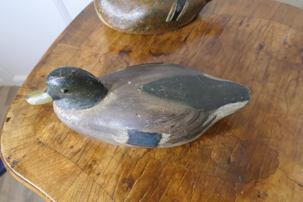 Three hand-carved and painted wooden decoy ducks with weathered finishes rest on a polished timber surface. View VIII