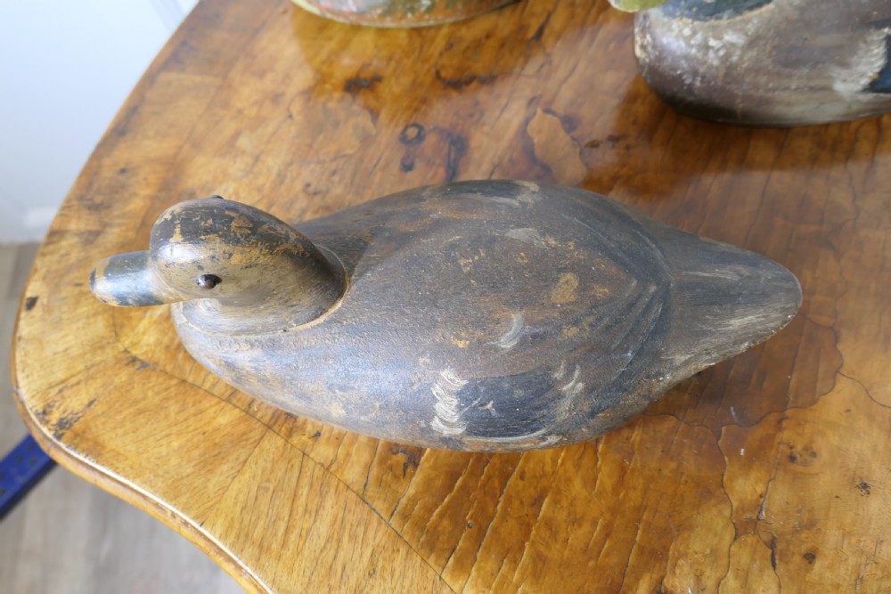 Three hand-carved and painted wooden decoy ducks with weathered finishes rest on a polished timber surface. View IX