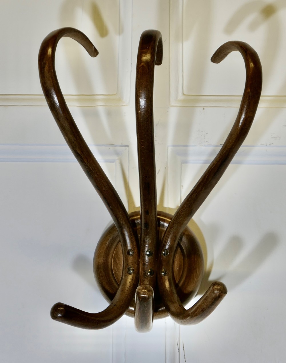 A dark brown bentwood wall-mounted coat rack featuring three sweeping upper hooks and three smaller lower hooks attached to a central circular base.