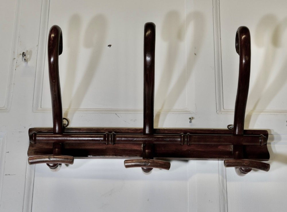 A dark brown wooden wall-mounted rack featuring three steam-bent coat and hat hooks secured to a horizontal backboard.