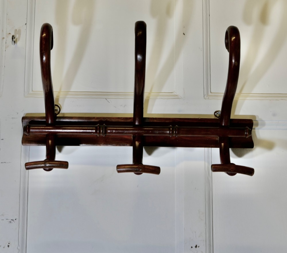 A dark brown wooden wall-mounted rack featuring three steam-bent coat and hat hooks secured to a horizontal backboard. View II