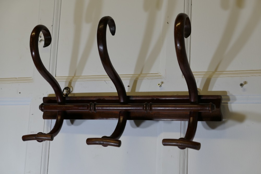 A dark brown wooden wall-mounted rack featuring three steam-bent coat and hat hooks secured to a horizontal backboard. View III