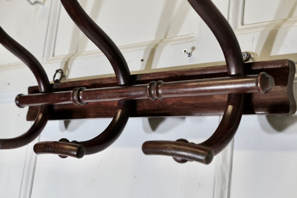 A dark brown wooden wall-mounted rack featuring three steam-bent coat and hat hooks secured to a horizontal backboard. View IV