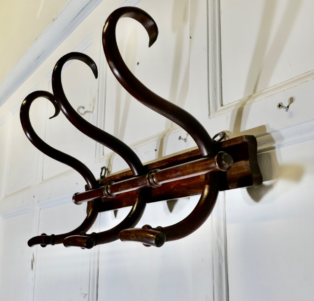 A dark brown wooden wall-mounted rack featuring three steam-bent coat and hat hooks secured to a horizontal backboard. View V