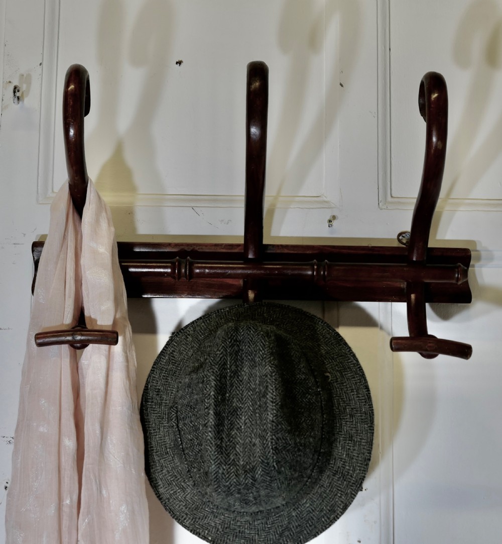 A dark brown wooden wall-mounted rack featuring three steam-bent coat and hat hooks secured to a horizontal backboard. View VI