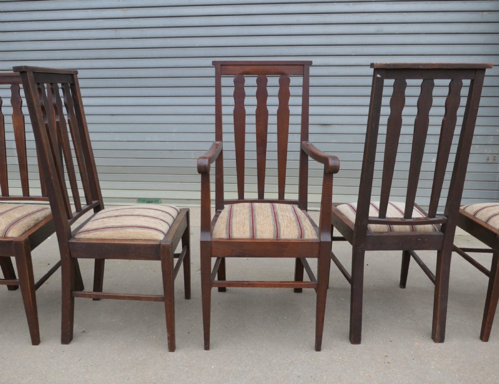 A set of six dark oak Arts and Crafts dining chairs featuring high vertical slat backs and striped fabric drop-in seats. View VI