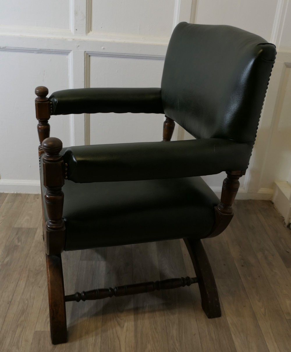 A 19th-century desk chair featuring dark green leather upholstery, brass stud detailing, turned arm supports, and a carved wooden X-frame base. View II