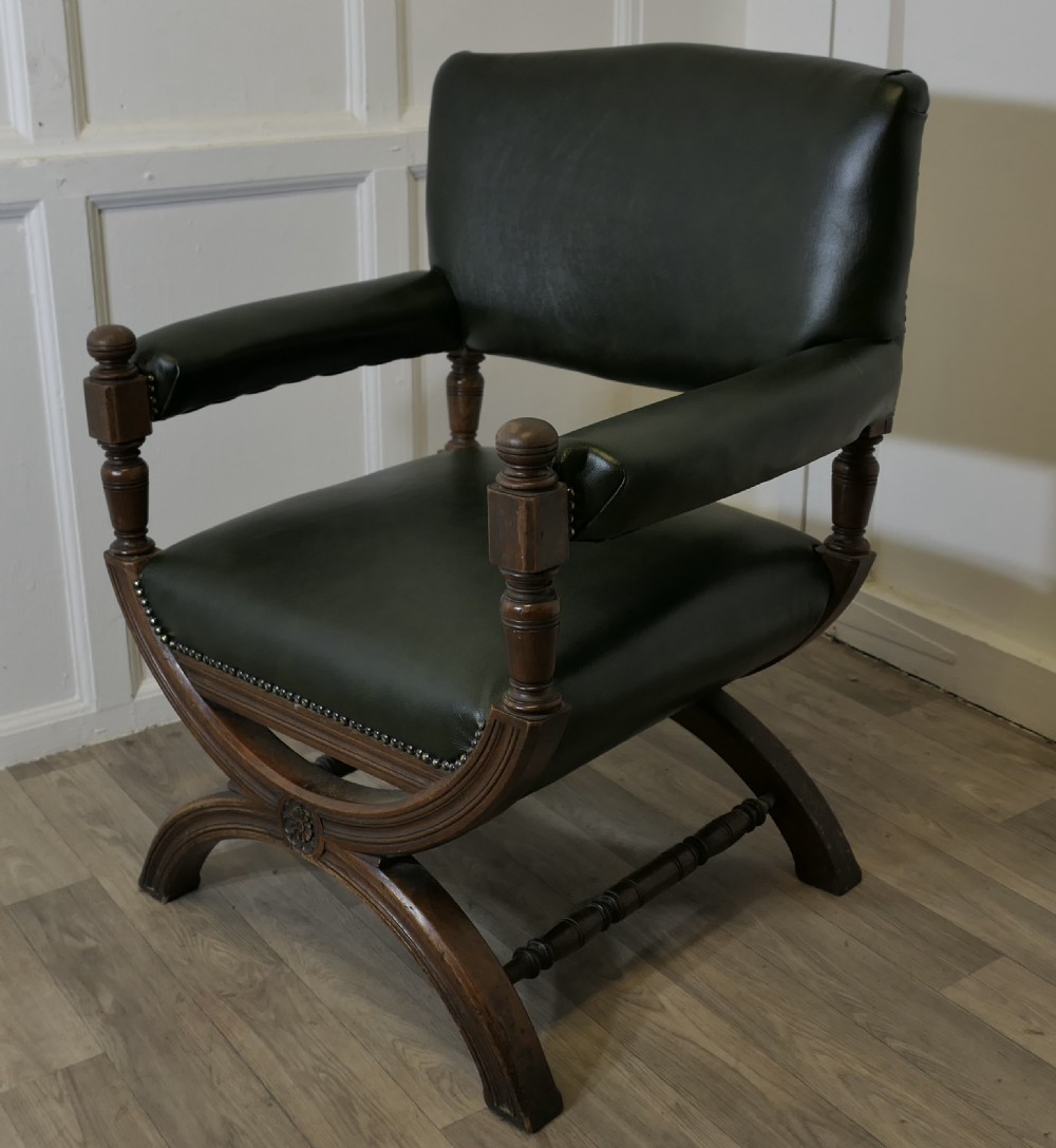 A 19th-century desk chair featuring dark green leather upholstery, brass stud detailing, turned arm supports, and a carved wooden X-frame base. View III