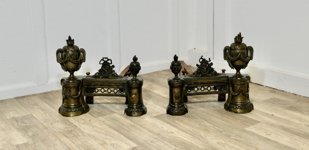 A pair of 18th-century French Neoclassical brass chenets featuring flame-topped urns, drapery swags, and pierced friezes supported on circular bases. View II