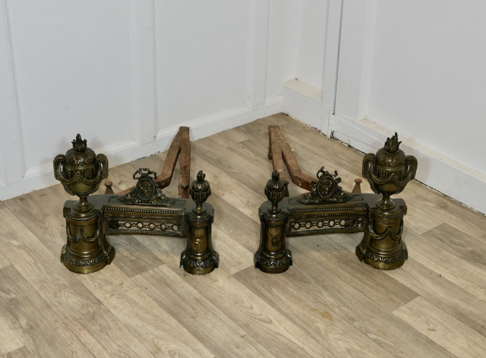 A pair of 18th-century French Neoclassical brass chenets featuring flame-topped urns, drapery swags, and pierced friezes supported on circular bases. View III