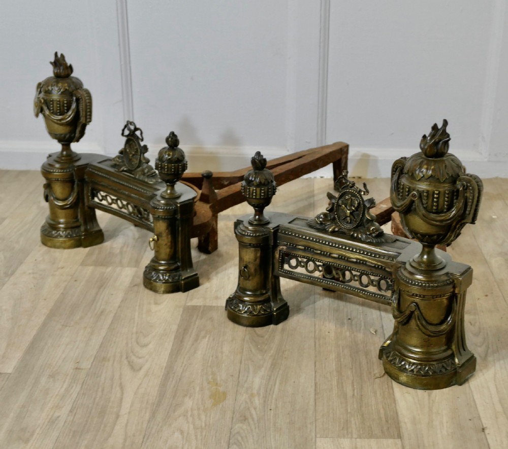 A pair of 18th-century French Neoclassical brass chenets featuring flame-topped urns, drapery swags, and pierced friezes supported on circular bases. View IV