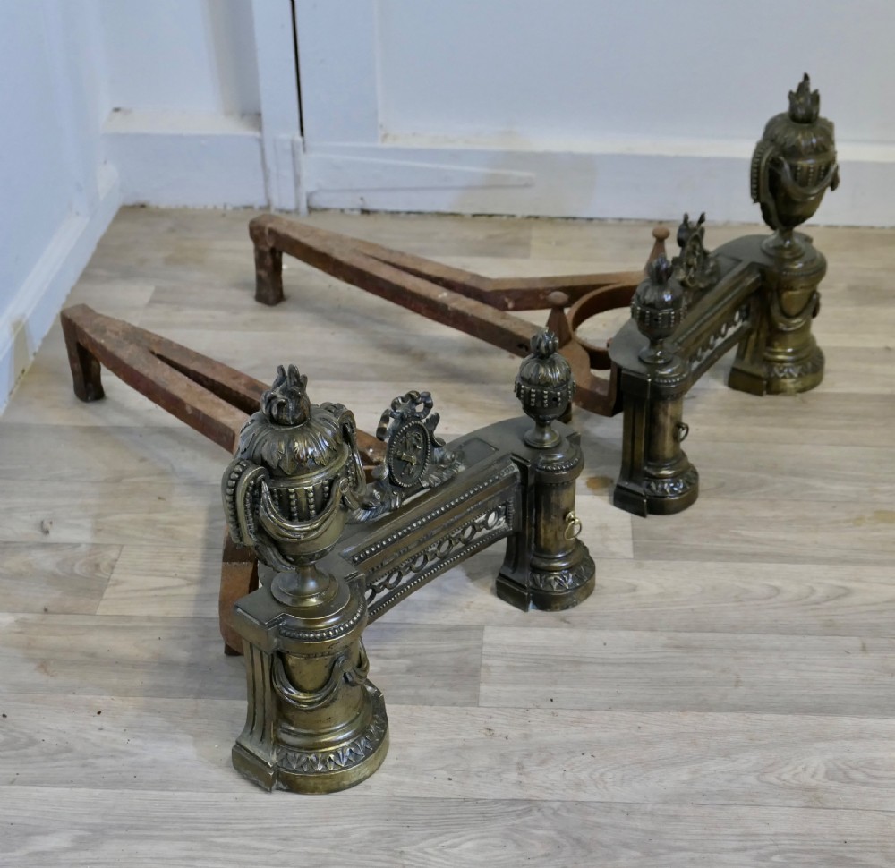 A pair of 18th-century French Neoclassical brass chenets featuring flame-topped urns, drapery swags, and pierced friezes supported on circular bases. View VI