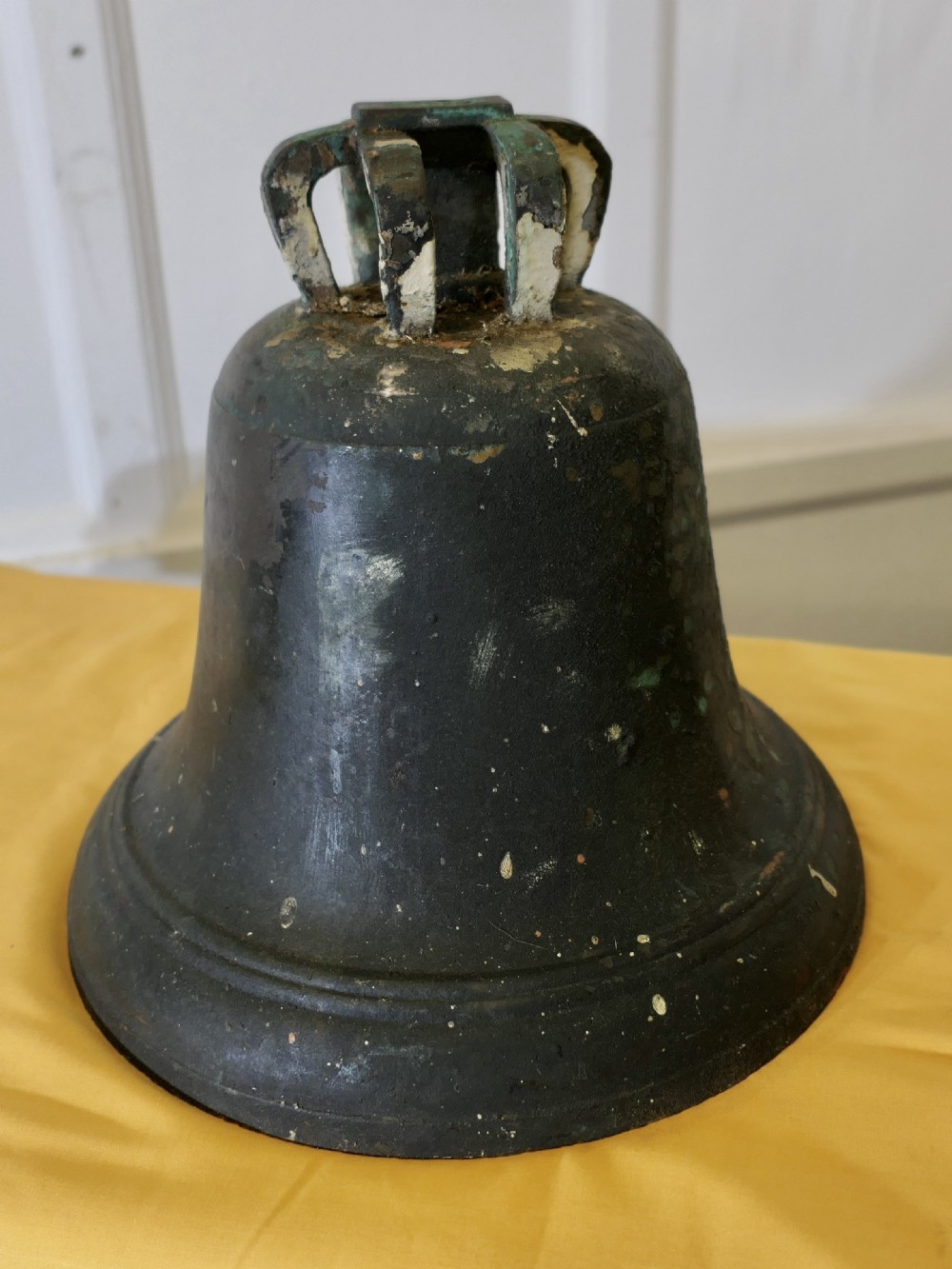 A heavy cast bronze tower bell with a dark weathered patina, white paint remnants, and arched crown loops at the top.