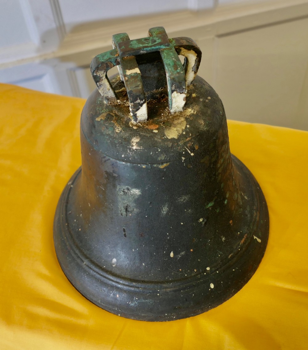 A heavy cast bronze tower bell with a dark weathered patina, white paint remnants, and arched crown loops at the top. View II