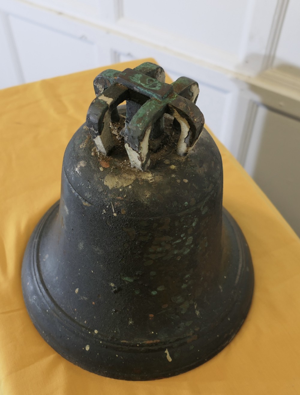 A heavy cast bronze tower bell with a dark weathered patina, white paint remnants, and arched crown loops at the top. View III