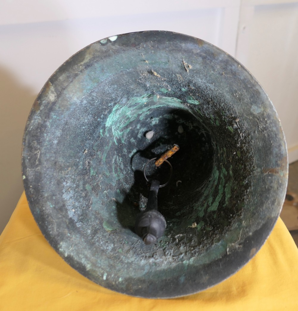 A heavy cast bronze tower bell with a dark weathered patina, white paint remnants, and arched crown loops at the top. View VI