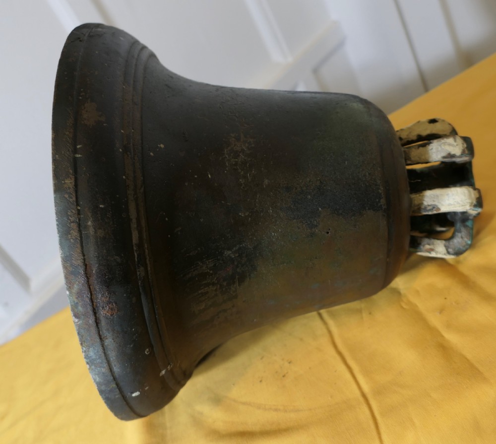 A heavy cast bronze tower bell with a dark weathered patina, white paint remnants, and arched crown loops at the top. View VII