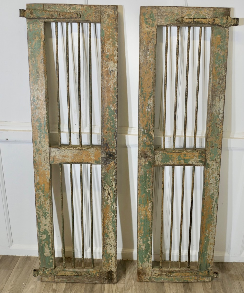 A pair of tall, rectangular antique wooden window shutters with vertical wrought iron bars and weathered green and ochre paint finish. View II