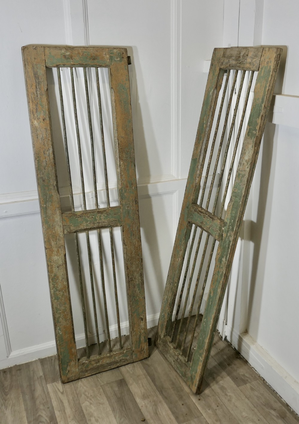 A pair of tall, rectangular antique wooden window shutters with vertical wrought iron bars and weathered green and ochre paint finish. View III