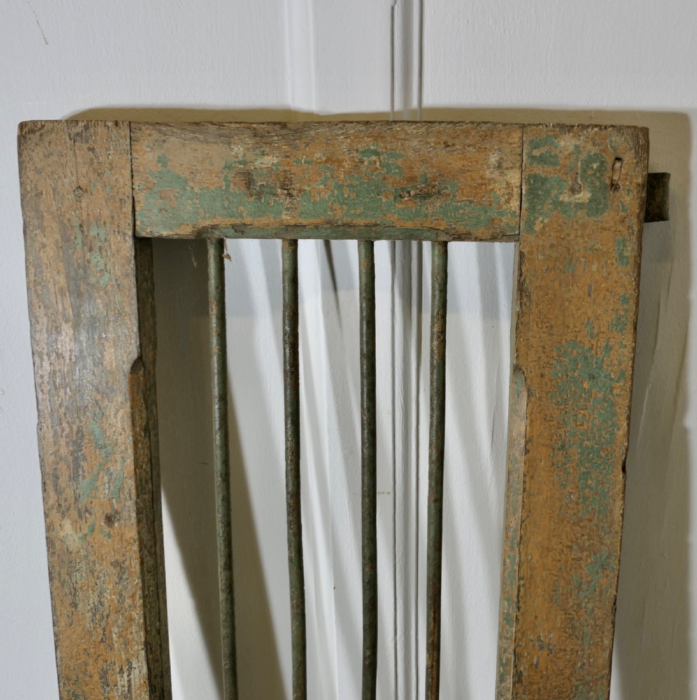 A pair of tall, rectangular antique wooden window shutters with vertical wrought iron bars and weathered green and ochre paint finish. View IV
