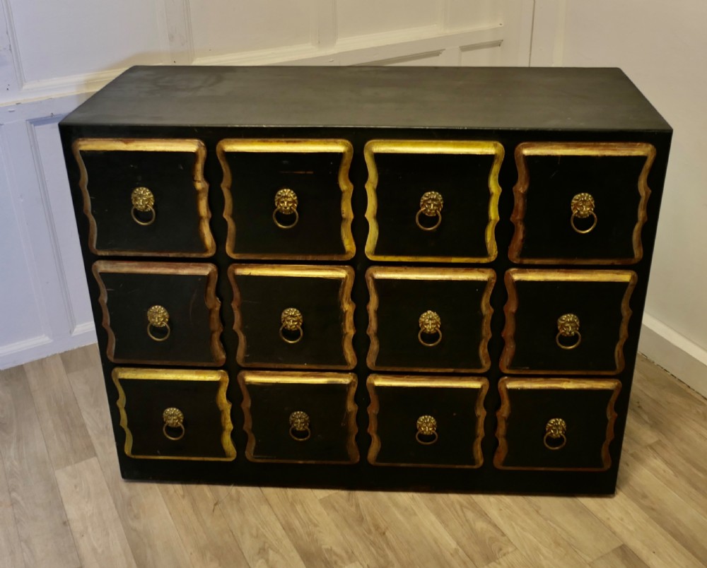 A black ebonised wooden chest featuring twelve small drawers detailed with contoured gold leaf borders and brass lion mask ring pulls. View II