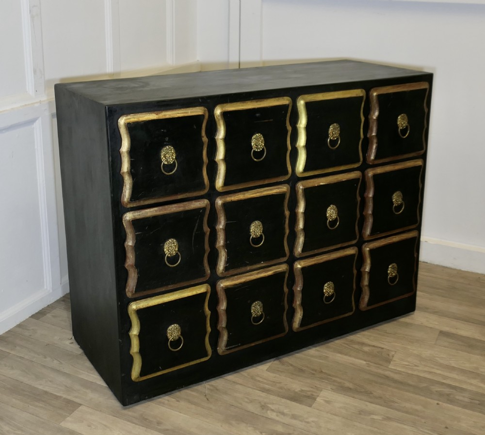 A black ebonised wooden chest featuring twelve small drawers detailed with contoured gold leaf borders and brass lion mask ring pulls. View III
