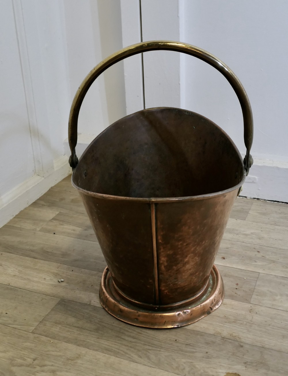 An antique hand-hammered copper helmet coal scuttle featuring a fixed brass overhead handle and riveted mounts. View III