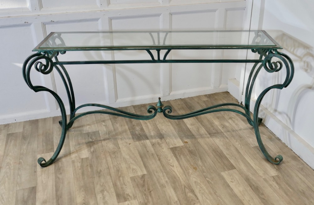 A green-painted wrought iron console table featuring curved scroll legs, a brass central finial, and a clear tabletop surface. View II