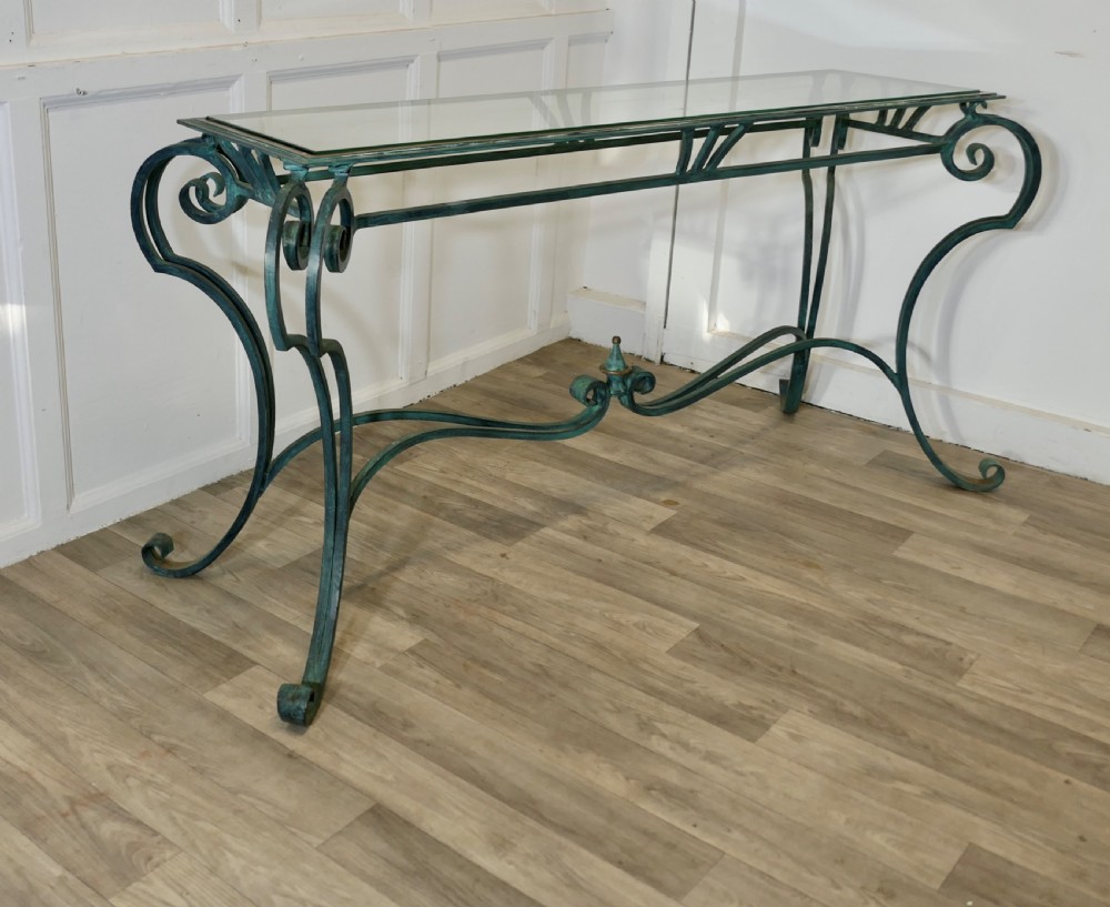 A green-painted wrought iron console table featuring curved scroll legs, a brass central finial, and a clear tabletop surface. View III