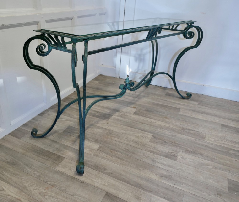 A green-painted wrought iron console table featuring curved scroll legs, a brass central finial, and a clear tabletop surface. View VIII