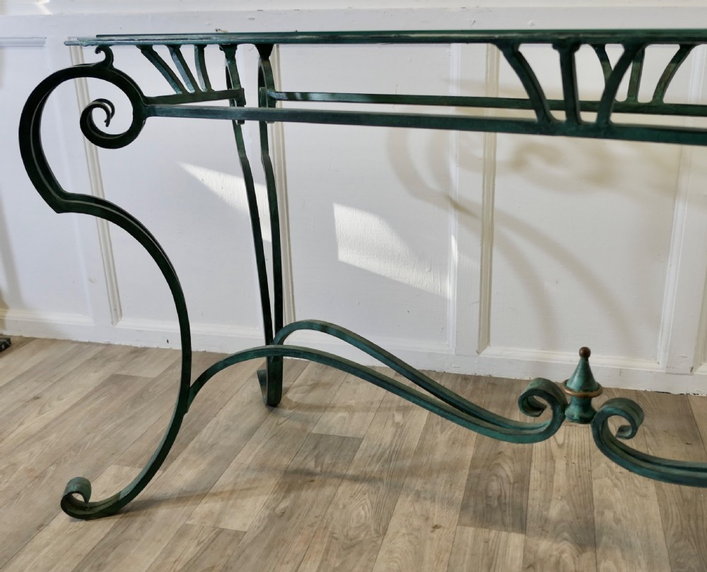A green-painted wrought iron console table featuring curved scroll legs, a brass central finial, and a clear tabletop surface. View XI