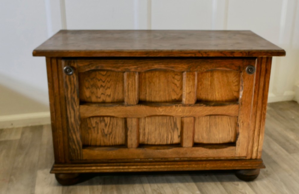 An Arts and Crafts golden oak low music cabinet with a rectangular top, six-panel fall-front door, round metal pulls, and turned feet.