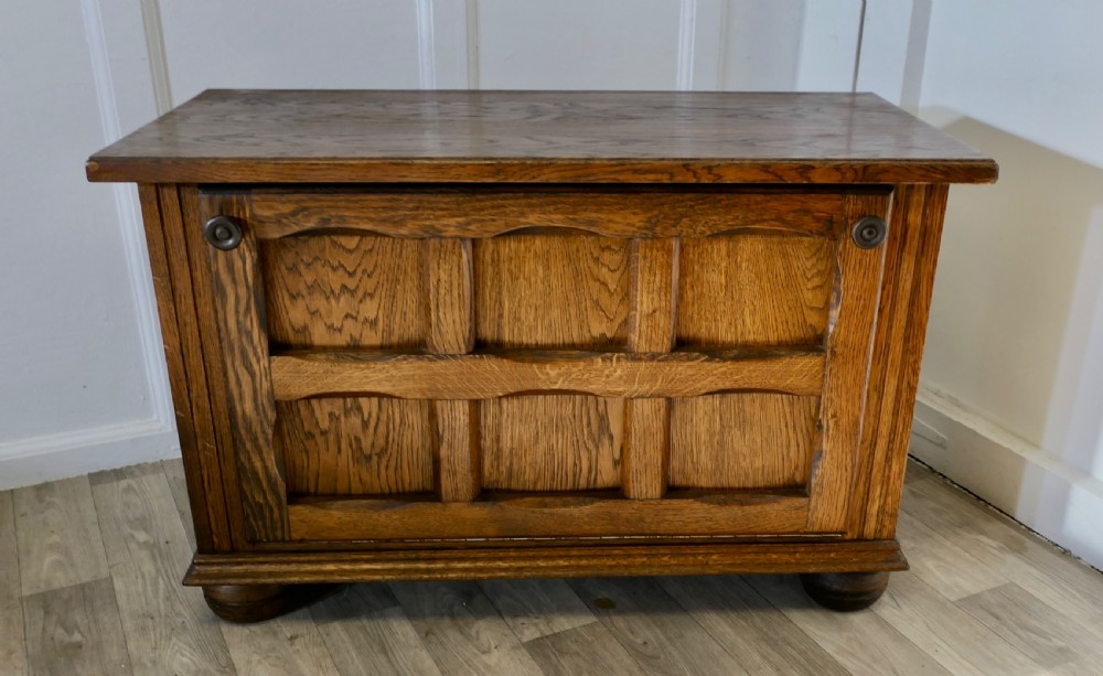 An Arts and Crafts golden oak low music cabinet with a rectangular top, six-panel fall-front door, round metal pulls, and turned feet. View II