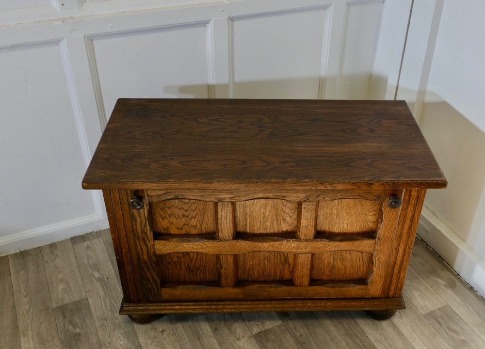 An Arts and Crafts golden oak low music cabinet with a rectangular top, six-panel fall-front door, round metal pulls, and turned feet. View III